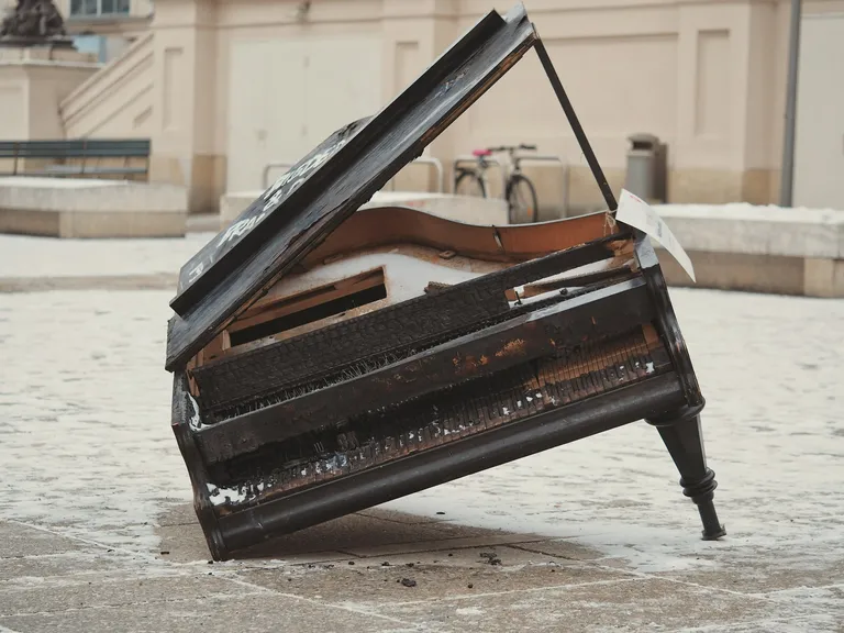 A photo by Adrian Swancar of a broken grand piano (missing a leg) on a street