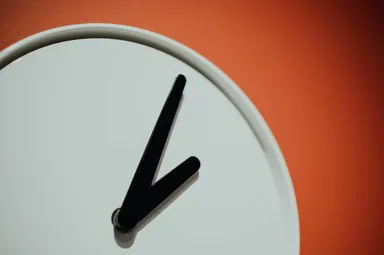 A photo by Chuttersnap of an analogue clock showing 2:05 against a burnt orange background