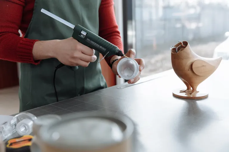 A photo by Thirdman of someone using a glue gun to assemble a model of a bird.