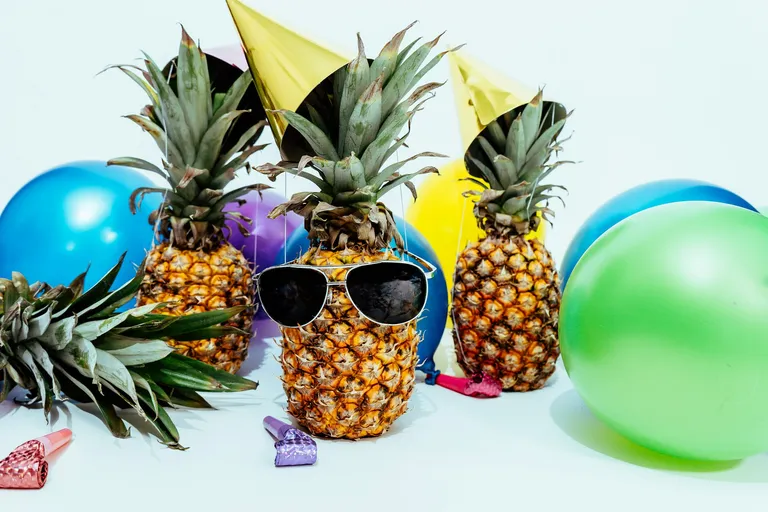 A photo by Scott Webb of three pineapples with party paraphernalia and sunglasses