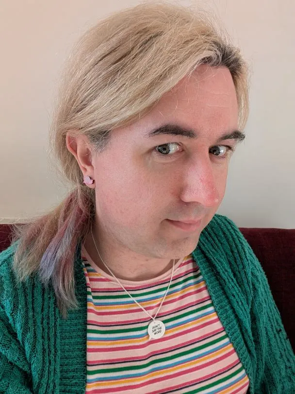 A smiling white transfeminine person with a stripy top and green cardigan