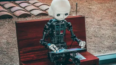 A photo by Andrea De Santis of a robot sat on a bench, ostensibly reading or working